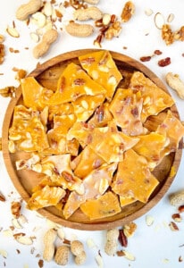 Quick & easy nut brittle, broken into pieces, on a round wooden board.