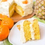 A slice of mandarin orange cake with pineapple frosting on a plate.