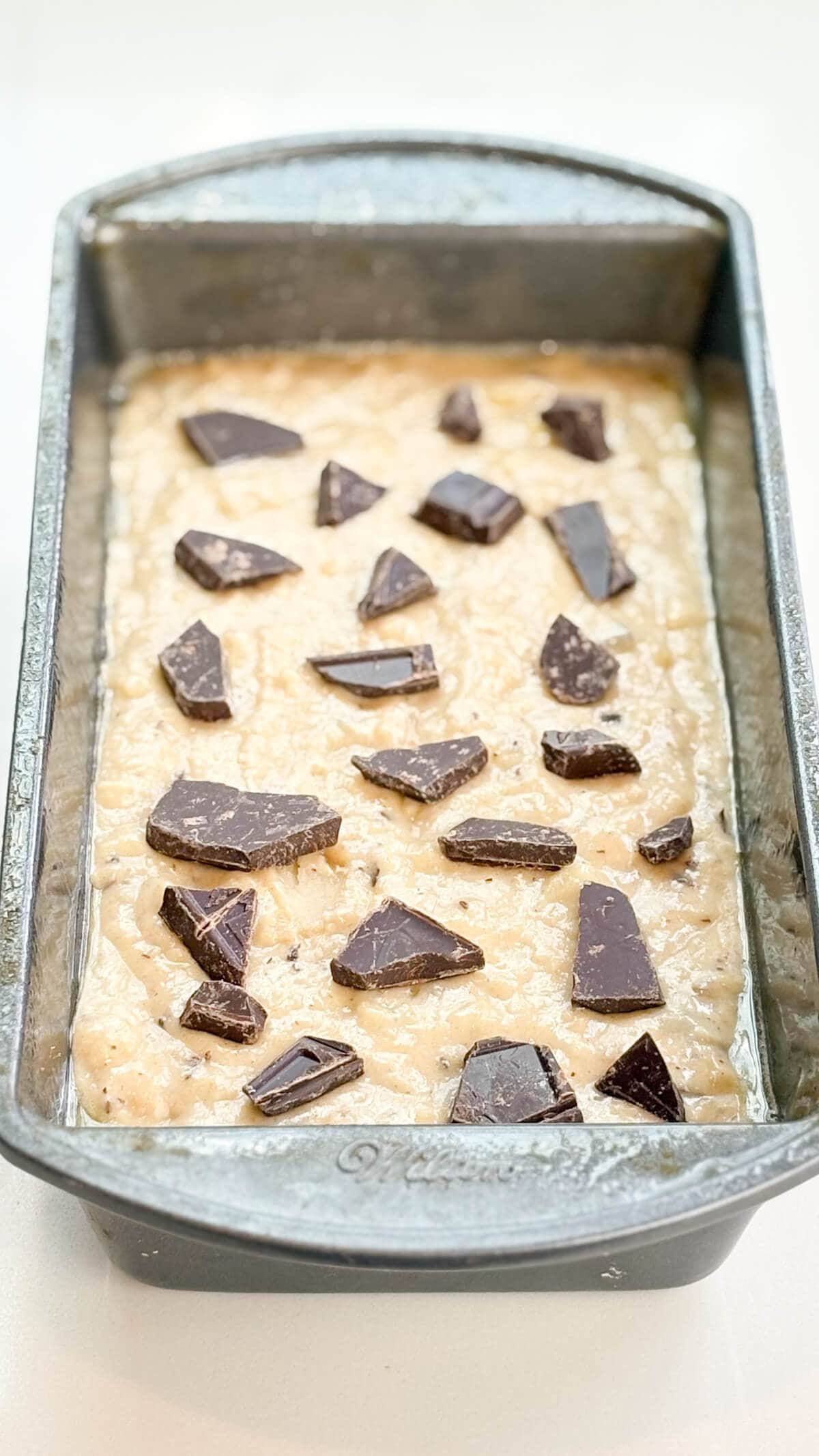 Batter in loaf pan with chocolate chunks on top.